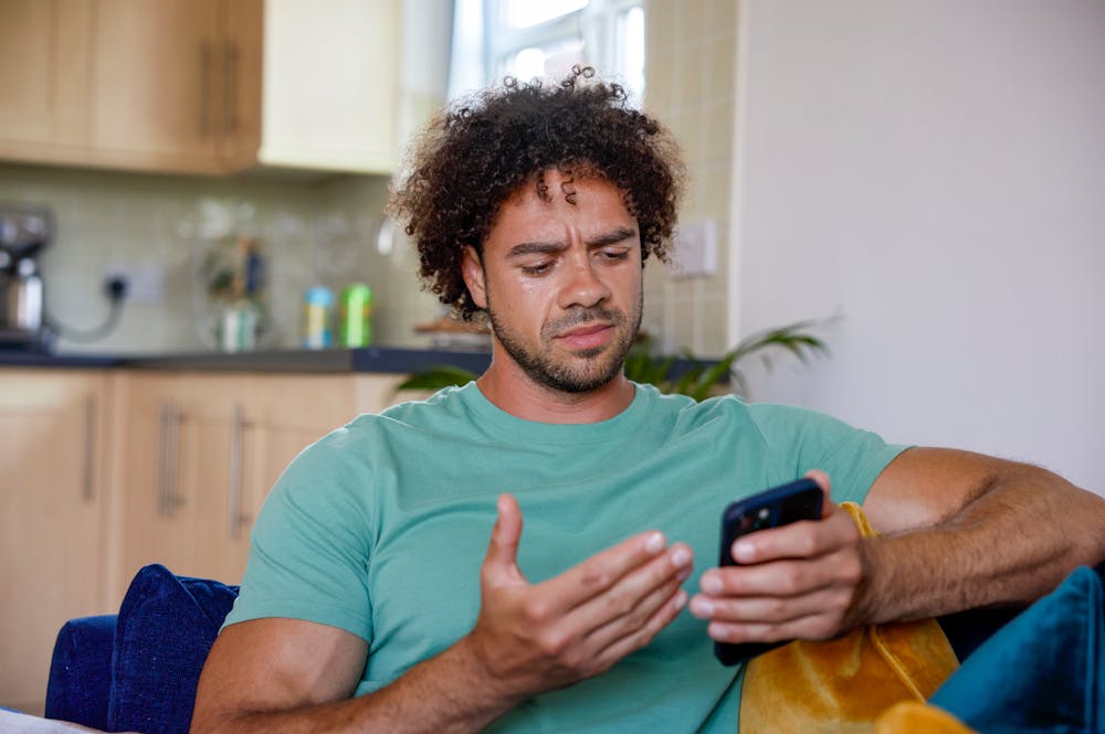 A close-up of a customer sitting on a sofa, holding their phone and looking confused at their screen.