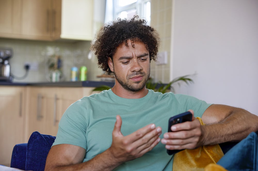 A close-up of a customer sitting on a sofa, holding their phone and looking confused at their screen.