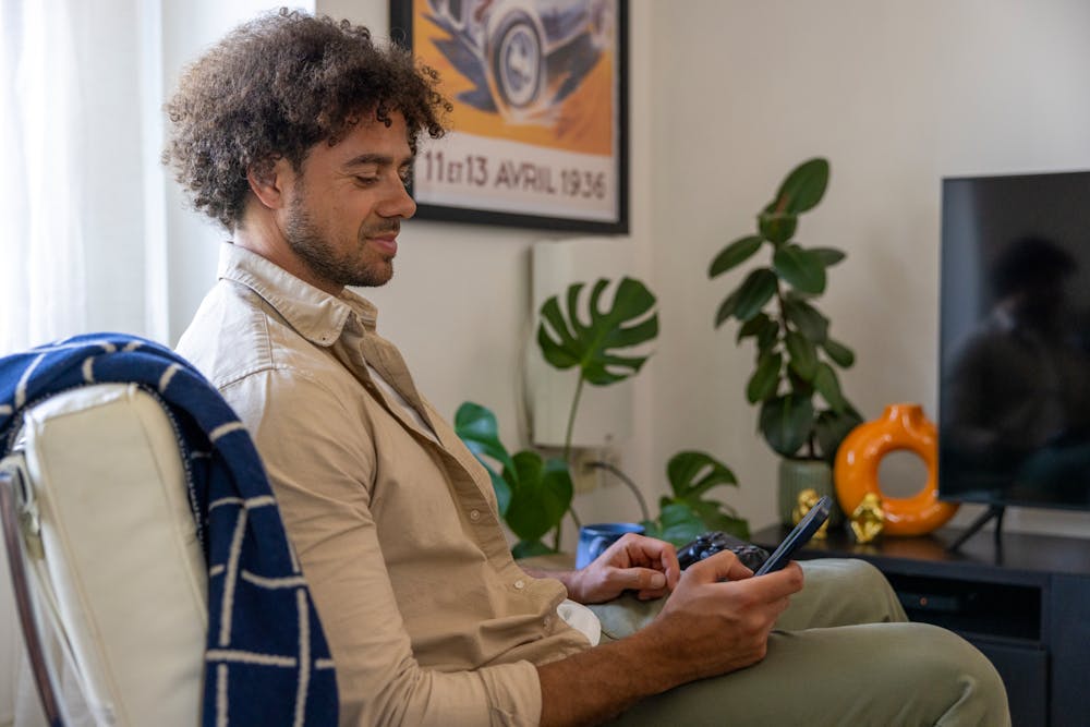 A side-profile view of a customer sitting on a sofa in their lounge, holding their mobile phone and looking at their screen.