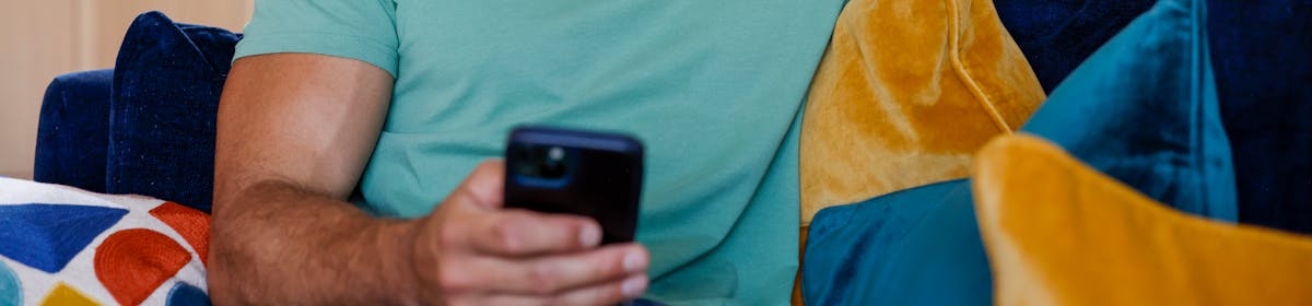 A close-up of a customer sitting on a sofa, holding their phone and smiling at their screen.