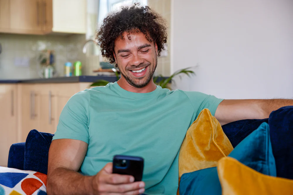 A close-up of a customer sitting on a sofa, holding their phone and smiling at their screen.