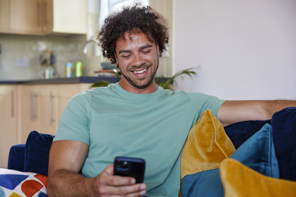 A close-up of a customer sitting on a sofa, holding their phone and smiling at their screen.
