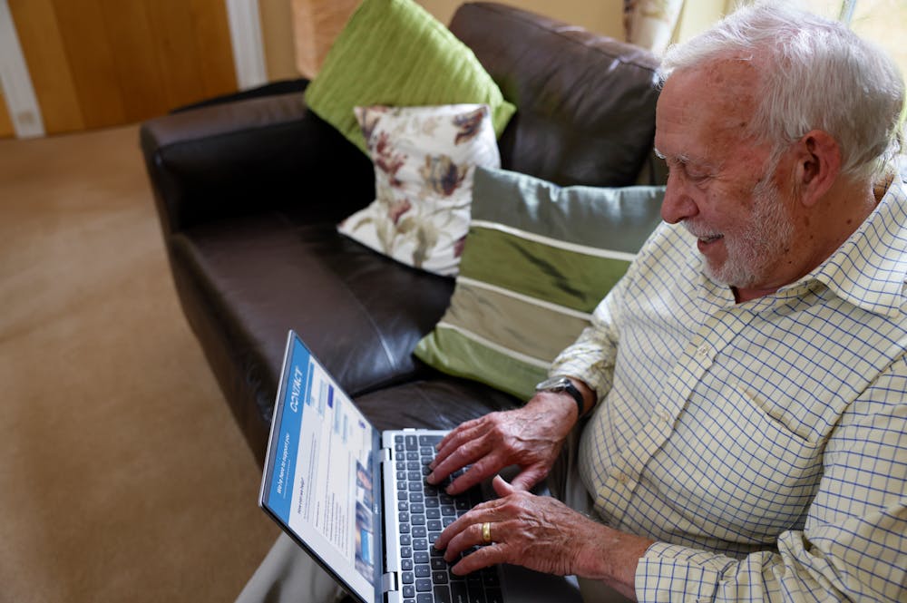 An older man is sat on a sofa with a laptop on his knee. The Evri website is visible on the screen. He looks happy.