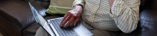 An older man is sat on a sofa with a laptop on his knee. The Evri website is visible on the screen. He looks deep in thought.