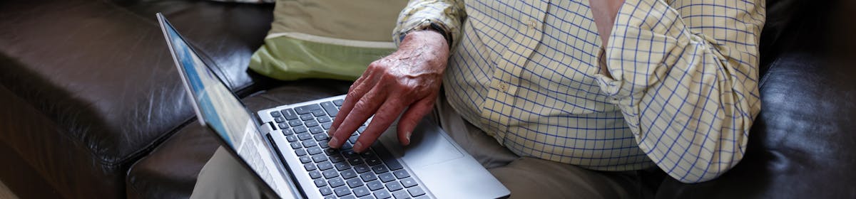 An older man is sat on a sofa with a laptop on his knee. The Evri website is visible on the screen. He looks deep in thought.