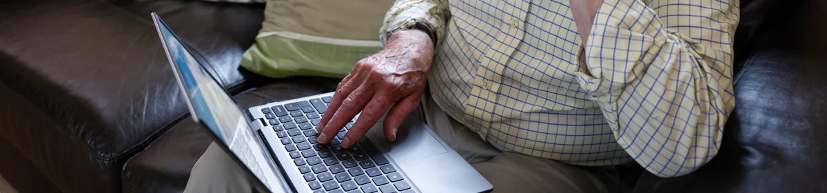 An older man is sat on a sofa with a laptop on his knee. The Evri website is visible on the screen. He looks deep in thought.