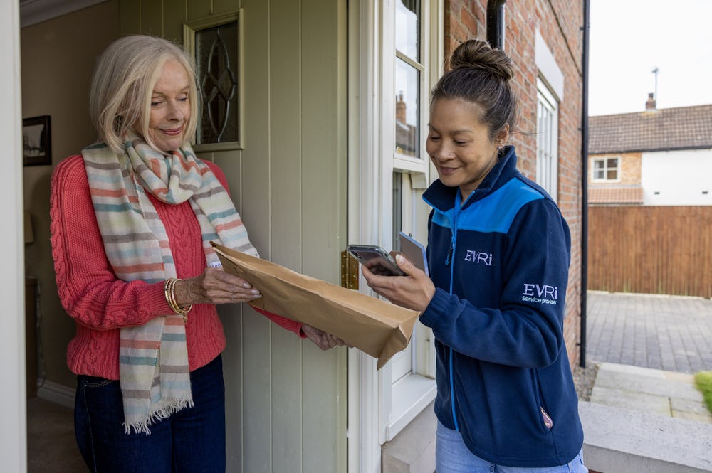 An older woman hands a parcel to a courier for collection. The courier is taking a photo.