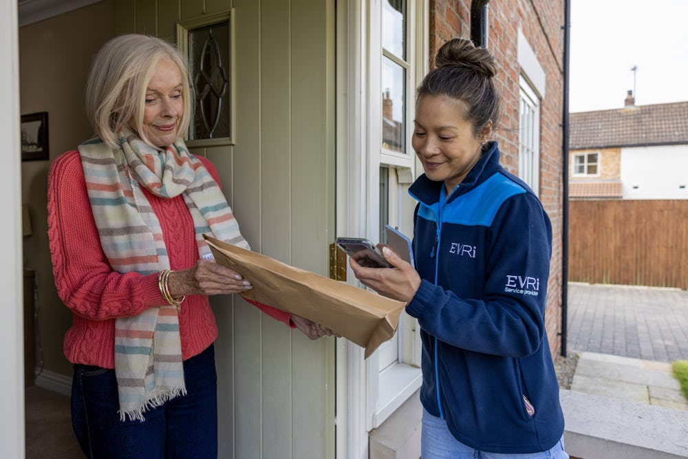 An older woman hands a parcel to a courier for collection. The courier is taking a photo.