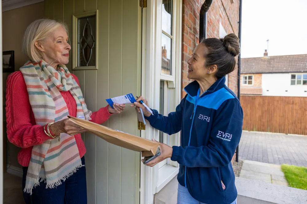 A courier is handing a blue collection receipt to an older woman at her door.