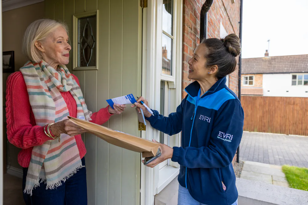 A courier is handing a blue collection receipt to an older woman at her door.