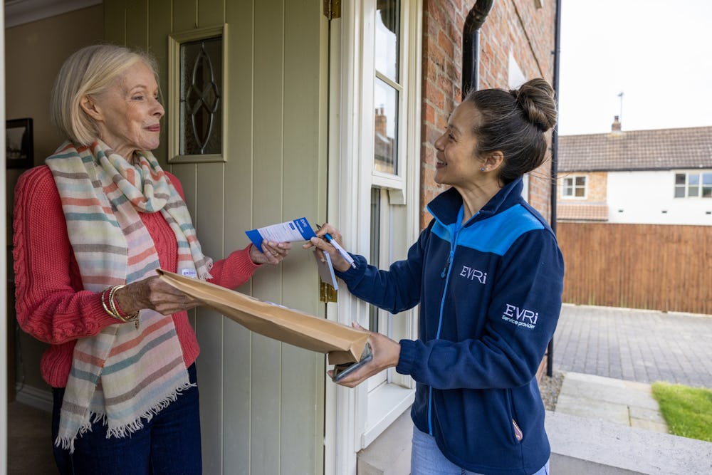 A courier is handing a blue collection receipt to an older woman at her door.