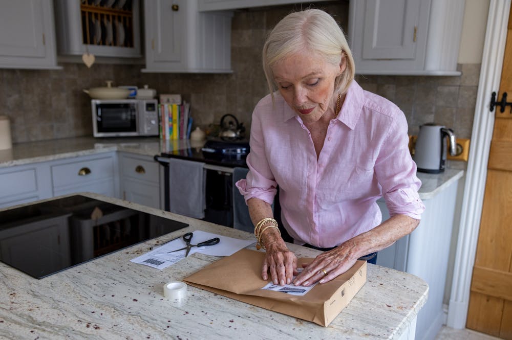 An older woman is wrapping a parcel. She is pressing down on the label to keep it flat.