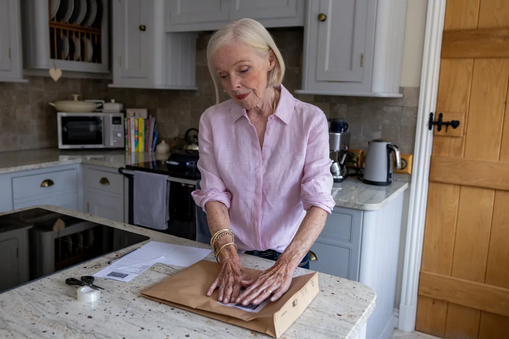 An older woman is wrapping a parcel. She is pressing down on the label to keep it flat.
