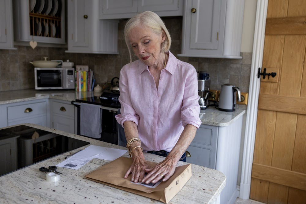 An older woman is wrapping a parcel. She is pressing down on the label to keep it flat.