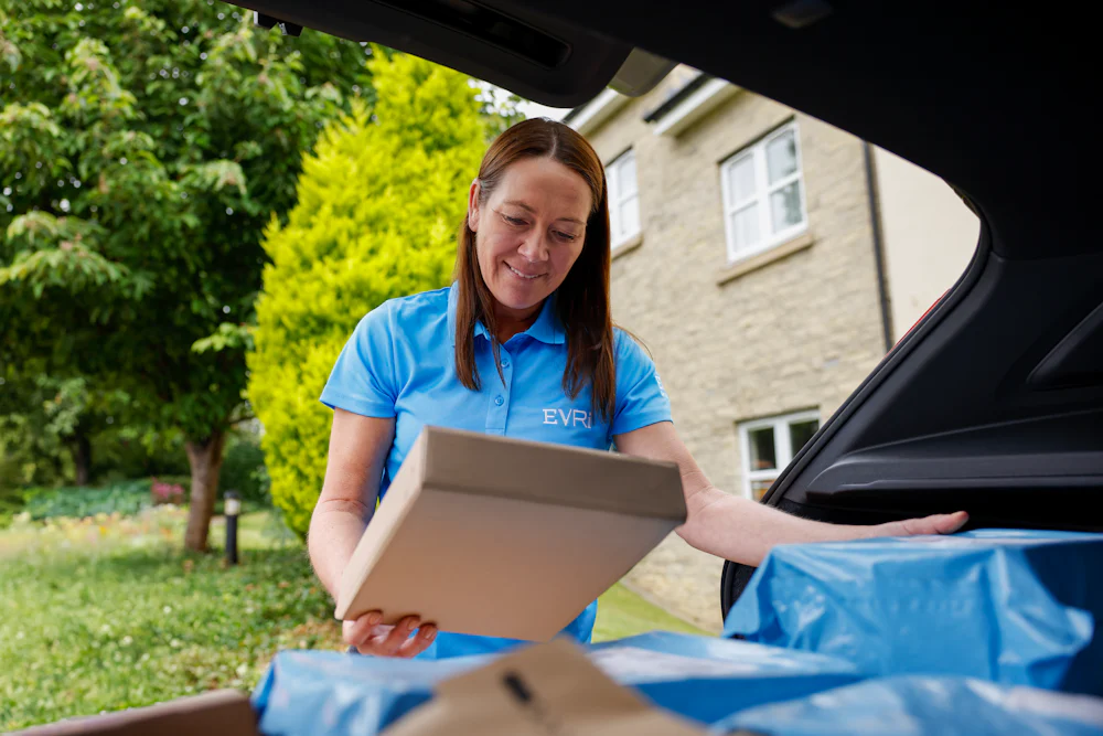 An Evri Courier checking the label on a parcel at their car before delivering