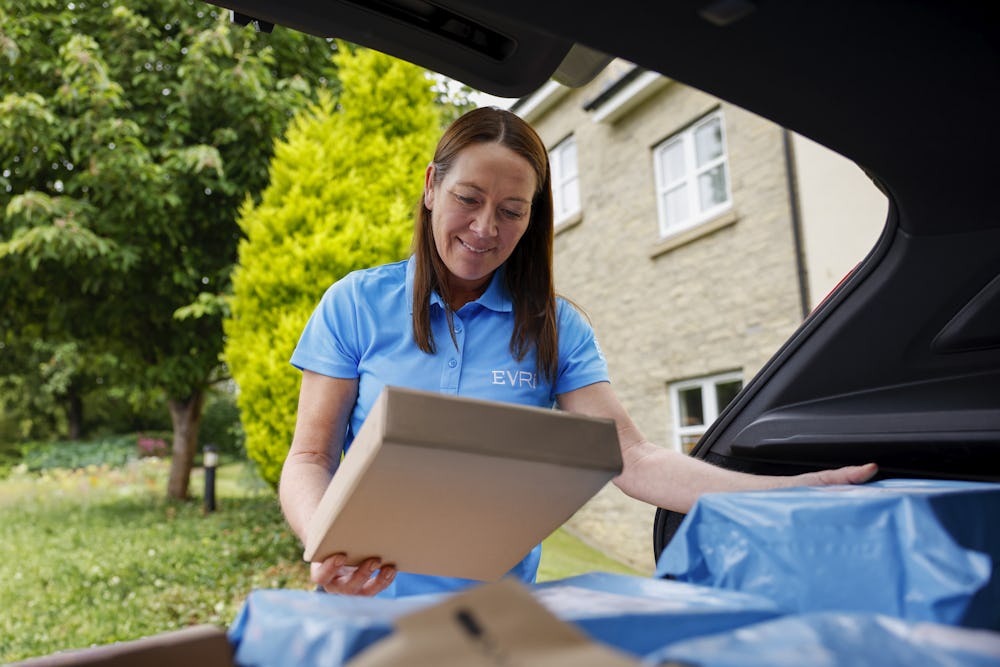 An Evri Courier checking the label on a parcel at their car before delivering