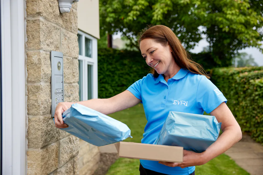 An Evri Courier delivering multiple parcels to a block of flats, checking the label before buzzing the recipients door