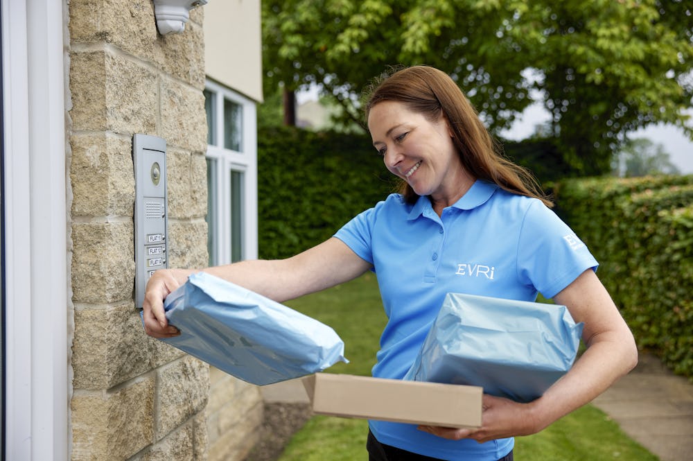 An Evri Courier delivering multiple parcels to a block of flats, checking the label before buzzing the recipients door
