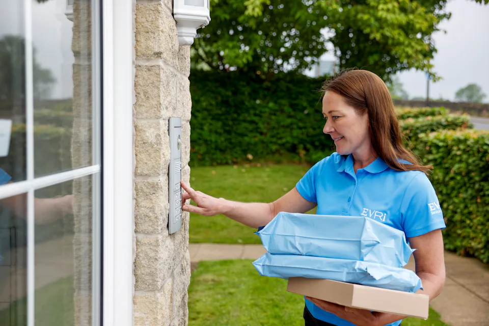 An Evri Courier delivering multiple parcels to a block of flats, pressing the buzzer to notify the recipient