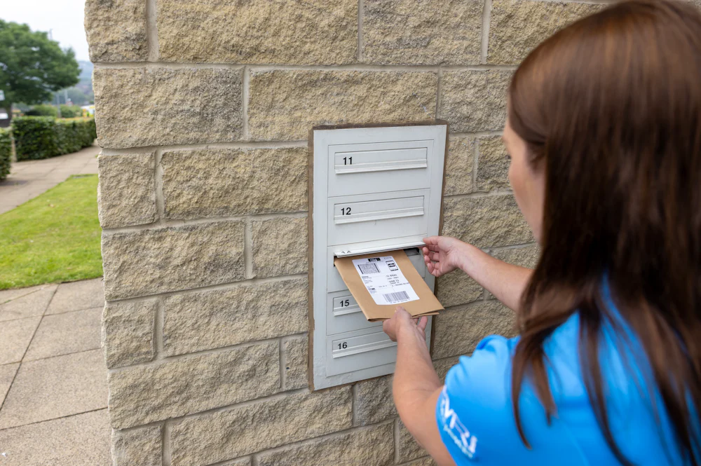 An Evri Courier delivering a postable parcel into the mailbox of a block of flats