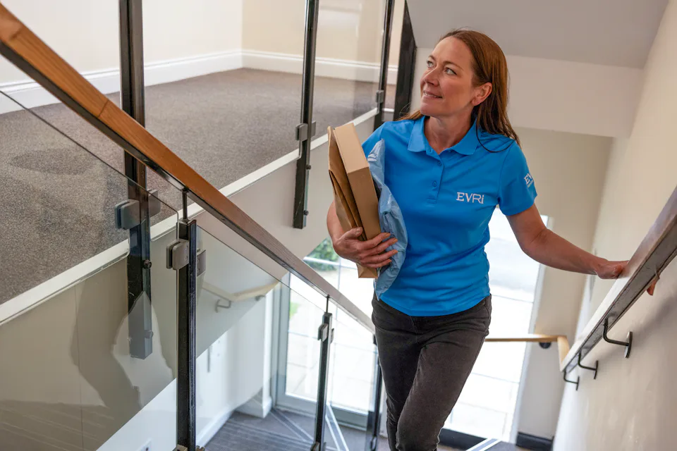 An Evri Courier climbing the stairs in a block of flats to deliver a parcel to a customers door