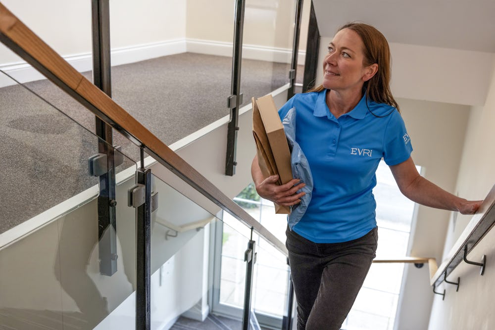 An Evri Courier climbing the stairs in a block of flats to deliver a parcel to a customers door