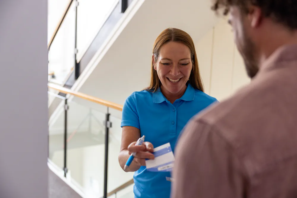 Following a doorstep collection in a block of flats, an Evri Courier is handing the customer a blue slip containing the details of the collection.