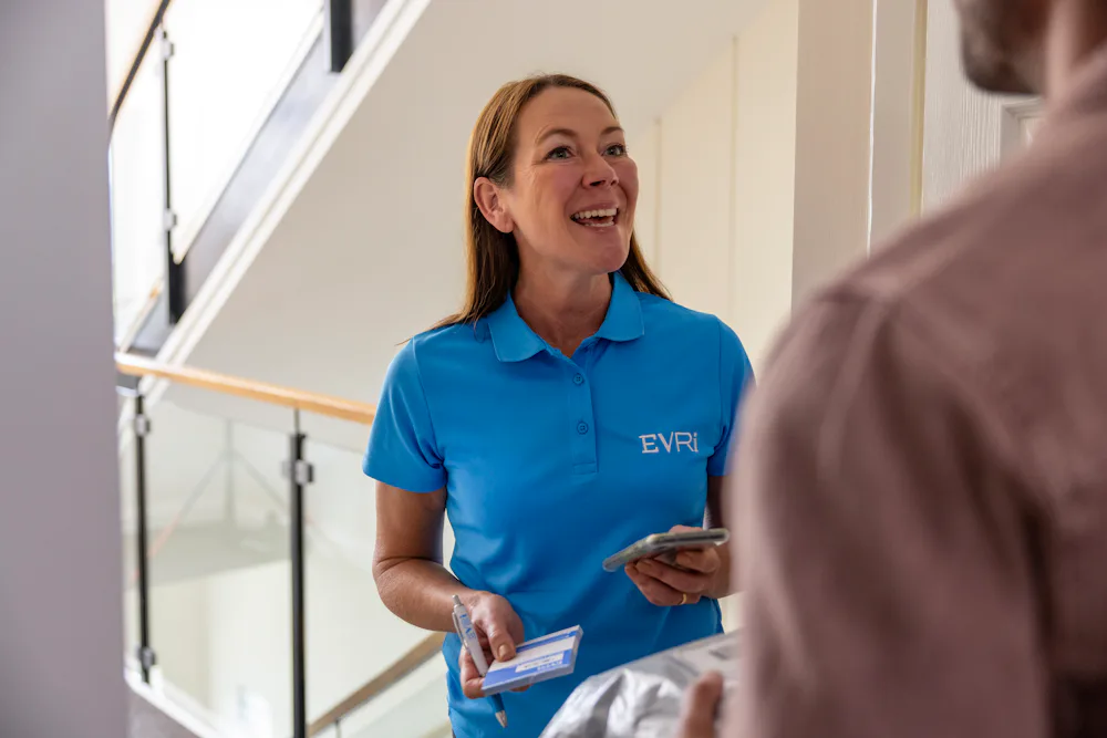 An Evri Courier greeting a customer as they begin a doorstep collection. The customer has their parcel ready to hand off, and the courier has a blue slip ready to record the collection.