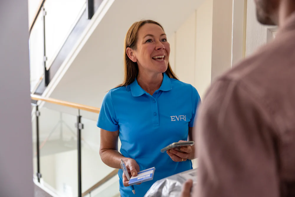 An Evri Courier greeting a customer as they begin a doorstep collection. The customer has their parcel ready to hand off, and the courier has a blue slip ready to record the collection.