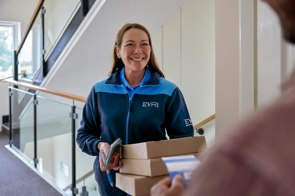 An Evri Courier smiling towards a customer after having completed a doorstep collection. The courier is holding multiple parcels, whilst the customer is holding a blue slip containing the details of the delivery.