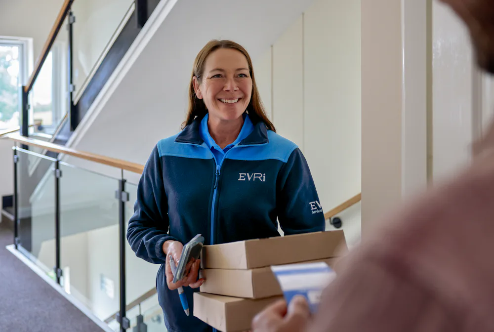 An Evri Courier smiling towards a customer after having completed a doorstep collection. The courier is holding multiple parcels, whilst the customer is holding a blue slip containing the details of the delivery.