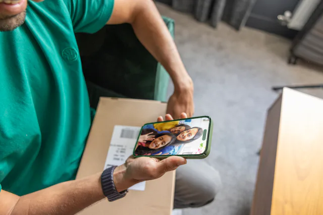 Top down view of a man with a parcel on his lap watching an Evri video. The video is of a mother and two children smiling and waving.