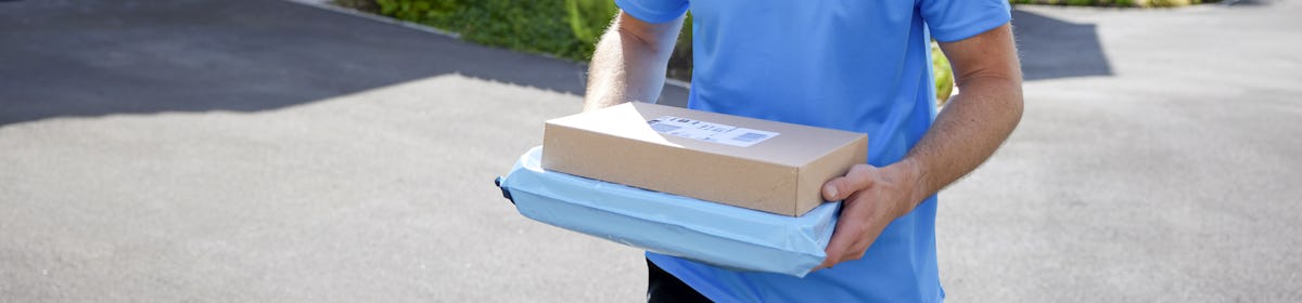 An Evri courier walking down a driveway in a suburban neighbourhood carrying two parcels.