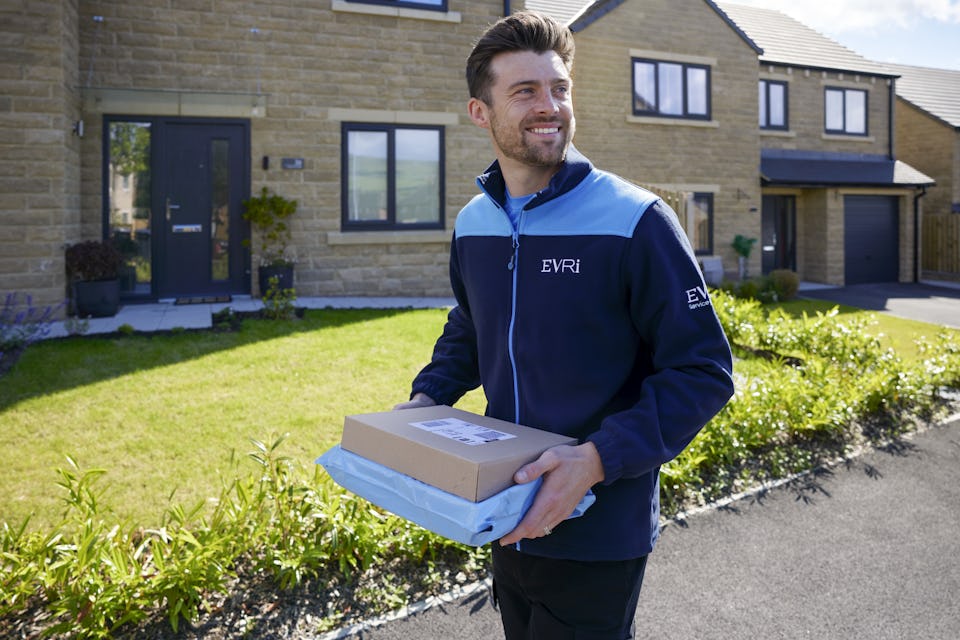 An Evri Courier walking down the street in a residential area carrying two parcels