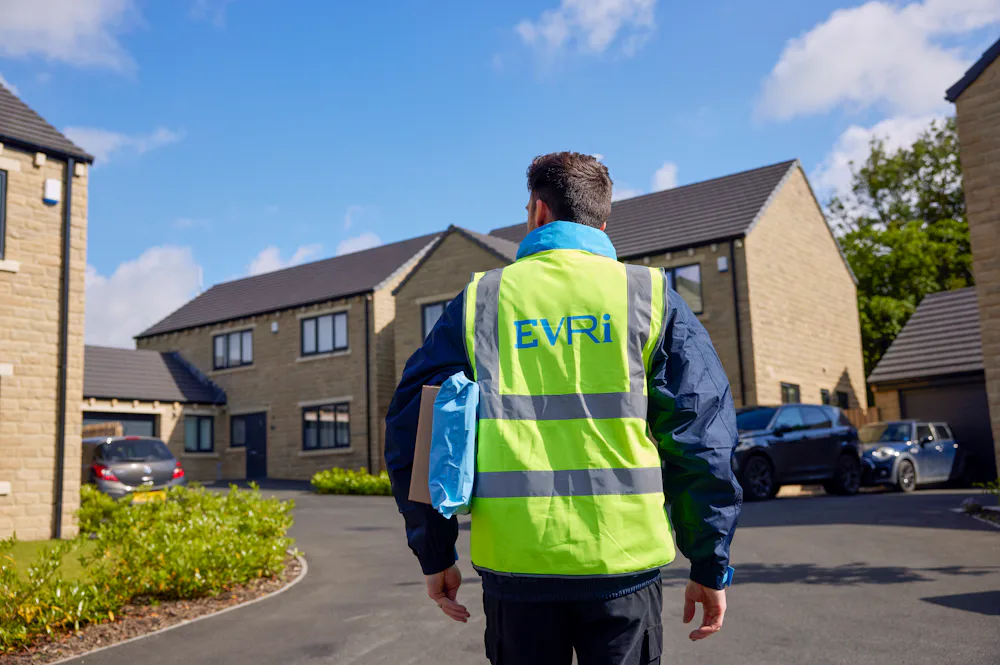An Evri Courier walking towards a row of houses in a residential area with two parcels under his arm