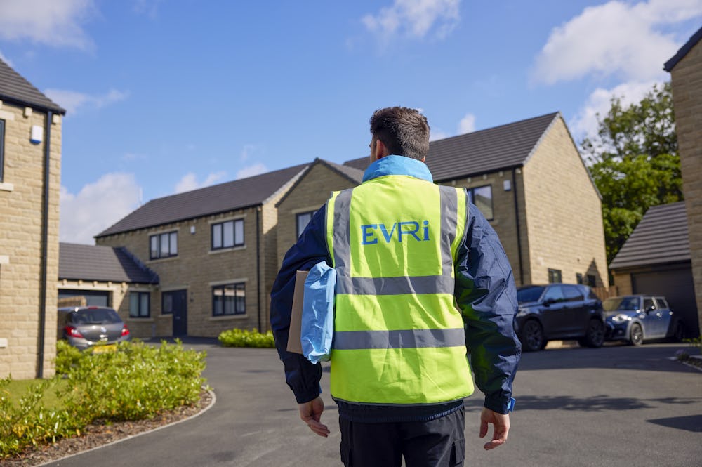 An Evri Courier walking towards a row of houses in a residential area with two parcels under his arm
