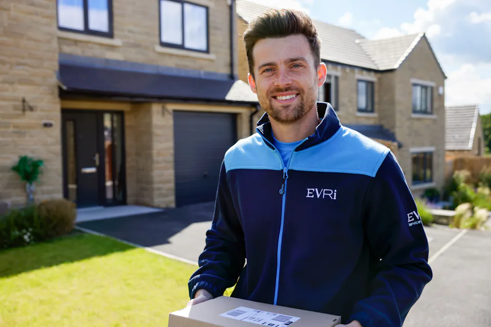 An Evri courier smiling and posing for the camera in a residential area holding a parcel.