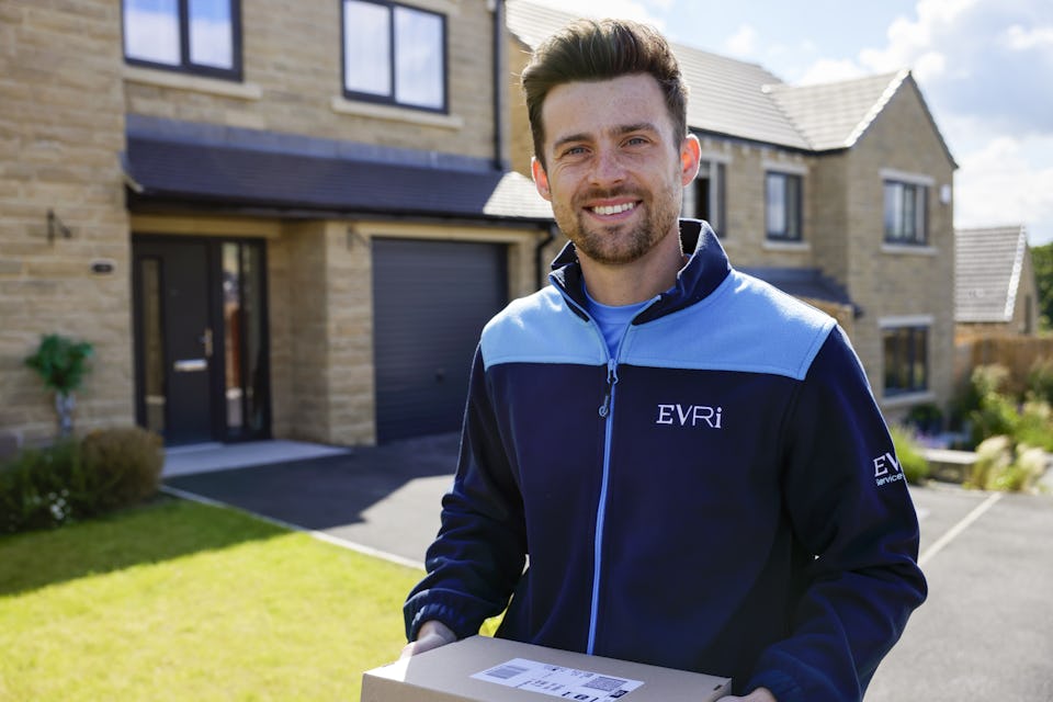 An Evri courier smiling and posing for the camera in a residential area holding a parcel.