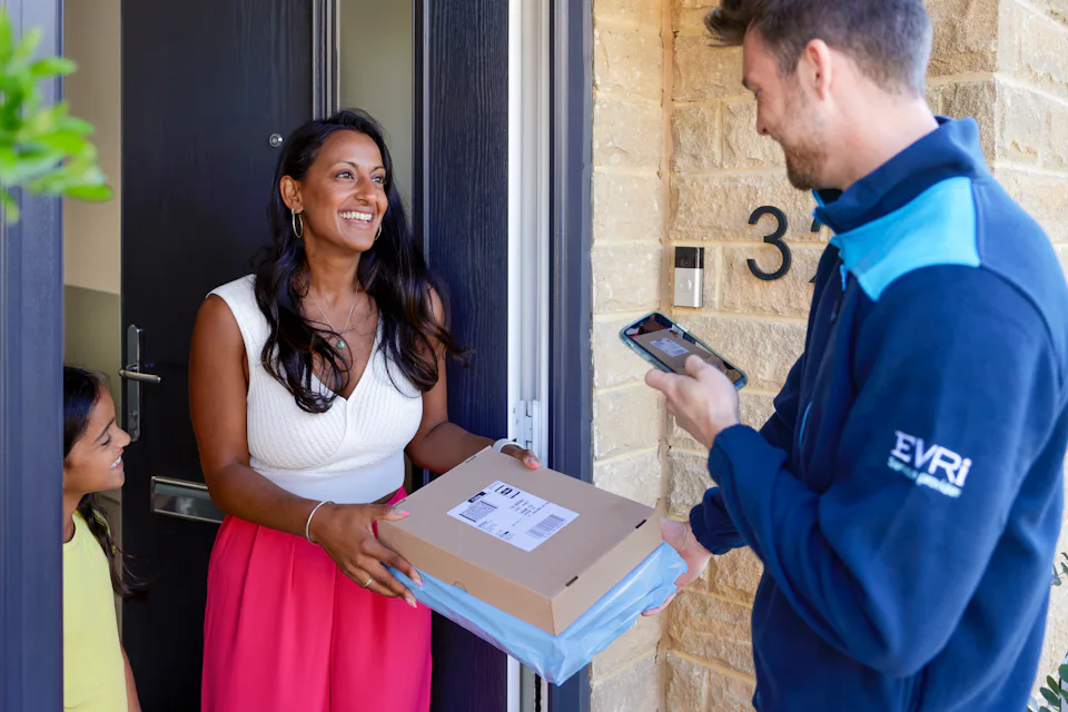 An Evri Courier delivering a parcel to an excited mother and child. The Courier is taking a photo for proof of delivery on their mobile device.