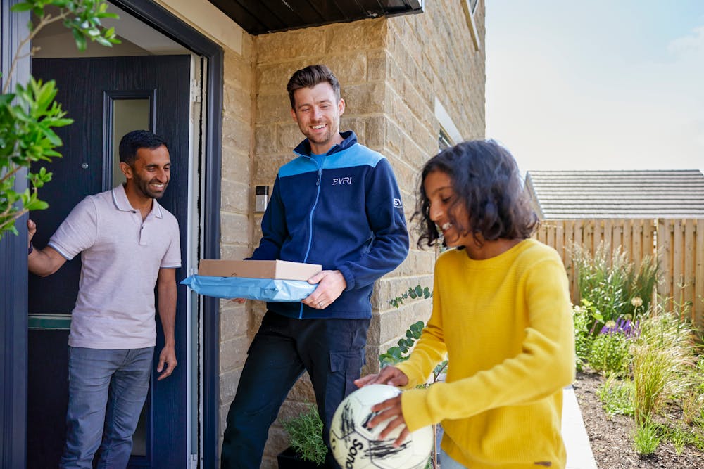 An Evri Courier about to deliver two parcels, and a customer ready to recieve them are being entertained by a child with a football.
