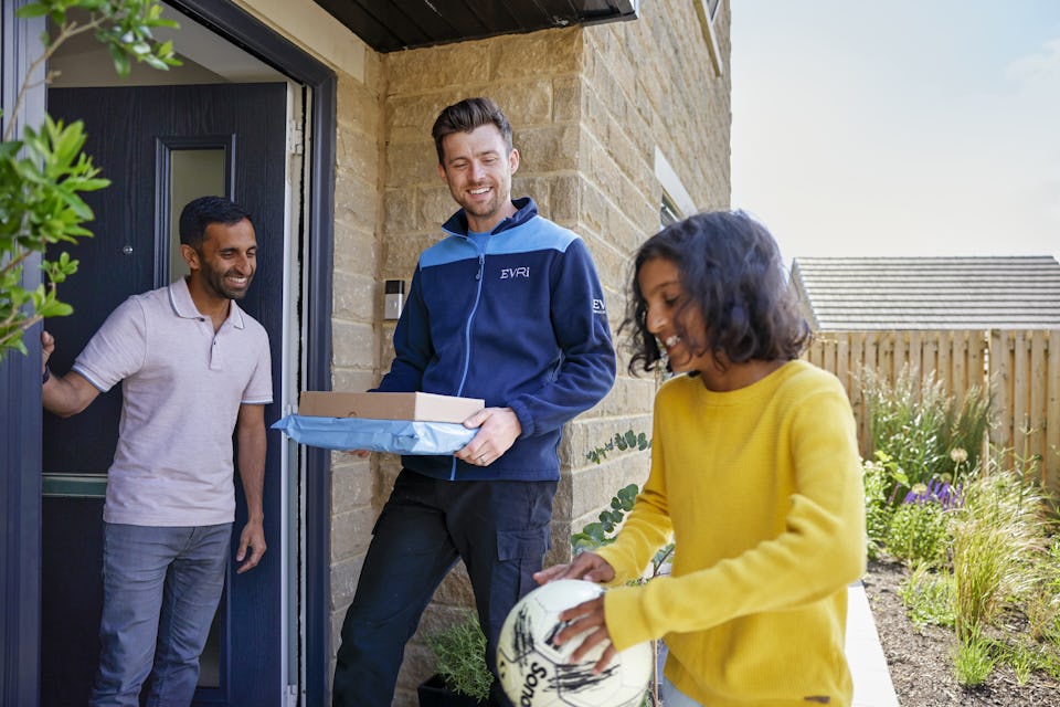 An Evri Courier about to deliver two parcels, and a customer ready to recieve them are being entertained by a child with a football.