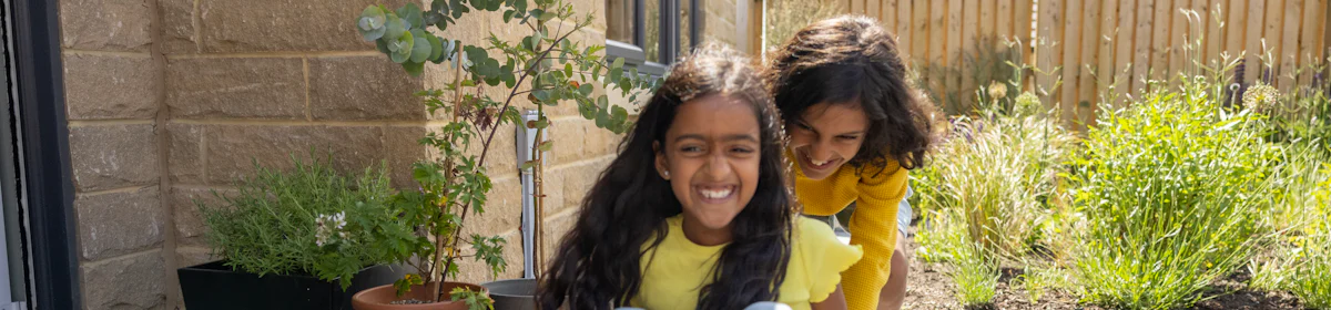 A child is pushing their sibling on a skateboard in front of their doorstep. They are both laughing and acting playful.