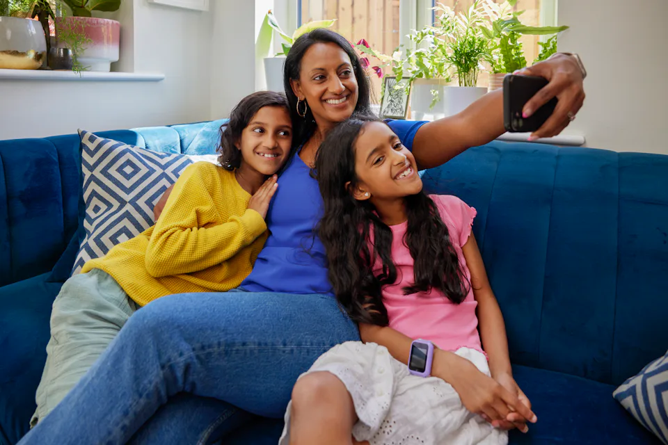 A mother and her two children record an Evri video on their mobile device. They are sat cuddled up on a sofa in their living room.