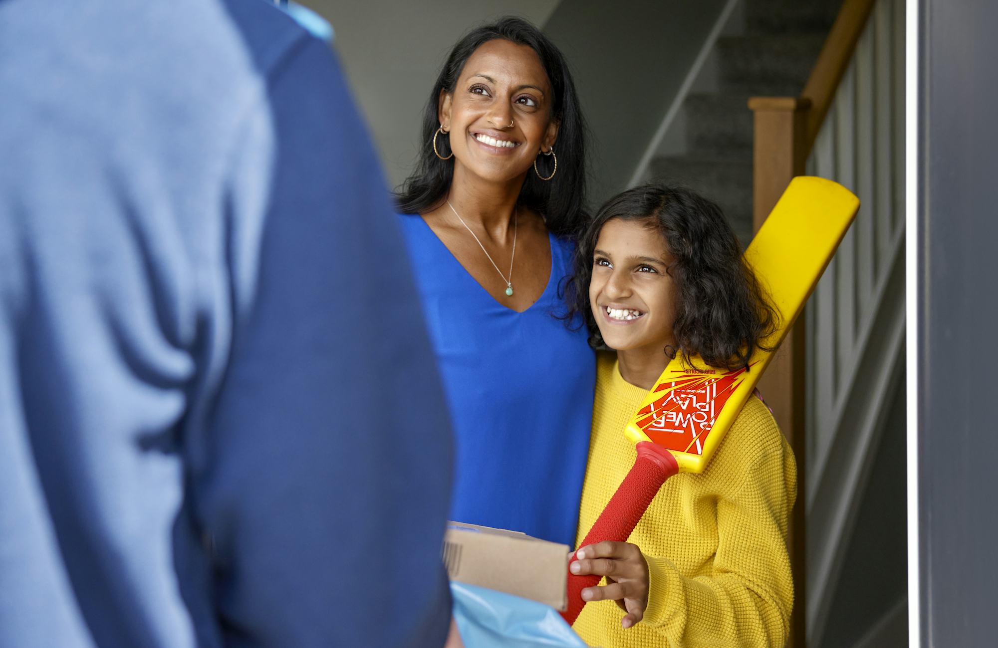 An Evri Courier is handing two parcels to a mother and child as they look very pleased towards the courier. The child is holding a cricket bat.