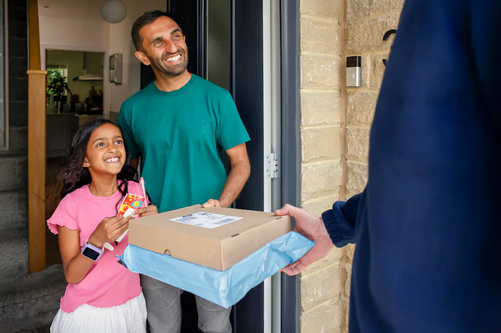 An Evri Courier is handing two parcels to a father and child as they look very pleased towards the courier.