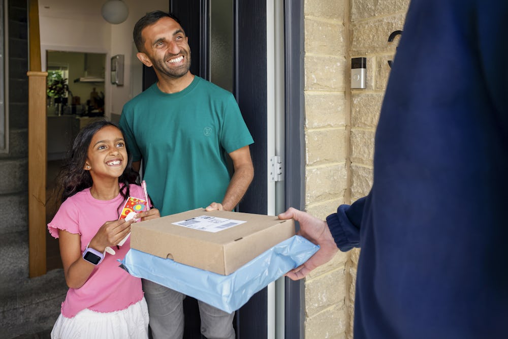 An Evri Courier is handing two parcels to a father and child as they look very pleased towards the courier.