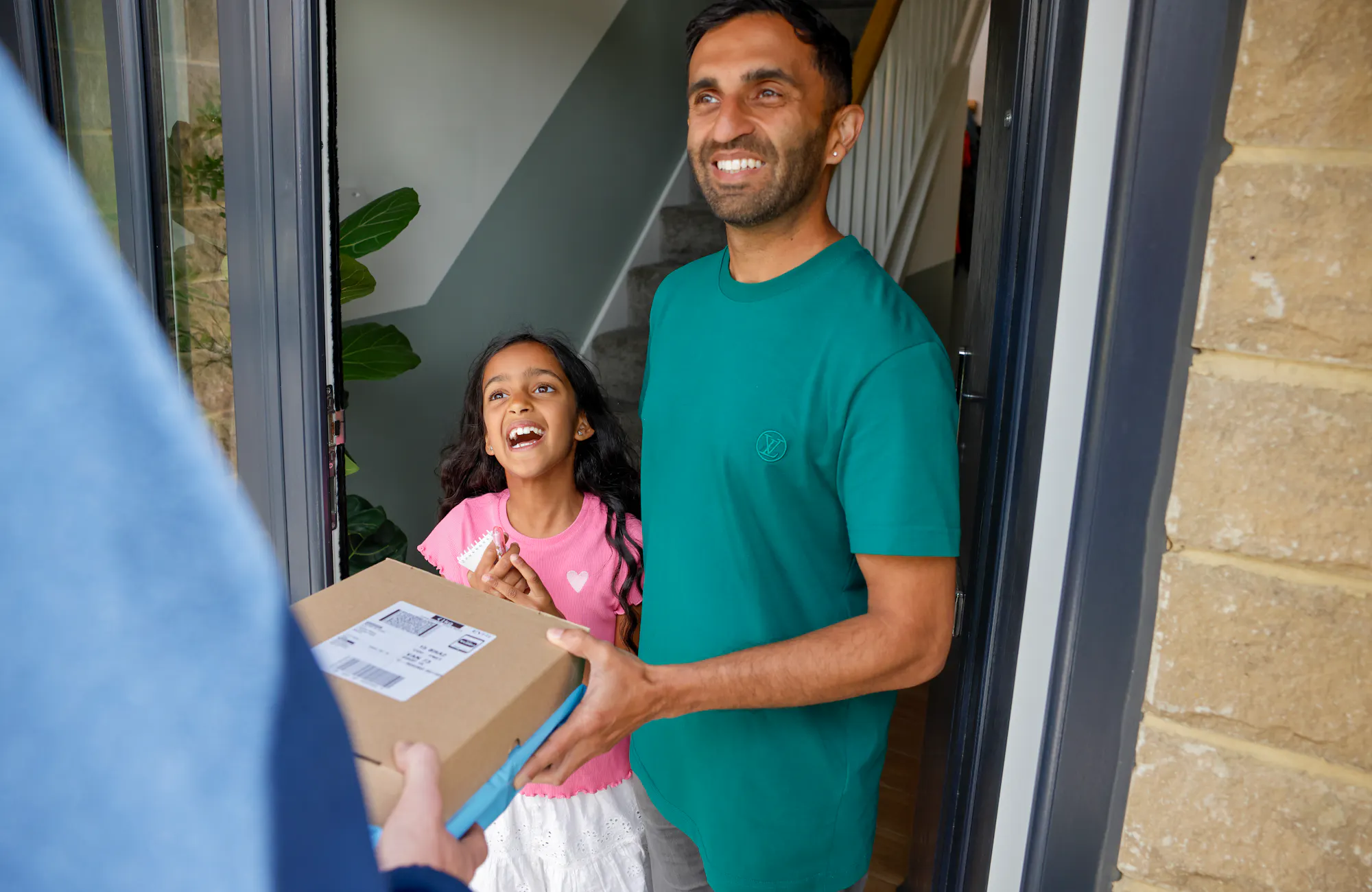 An Evri Courier is handing two parcels to a father and child on their doorstep. They are laughing as if a joke or anecdote was exchanged.