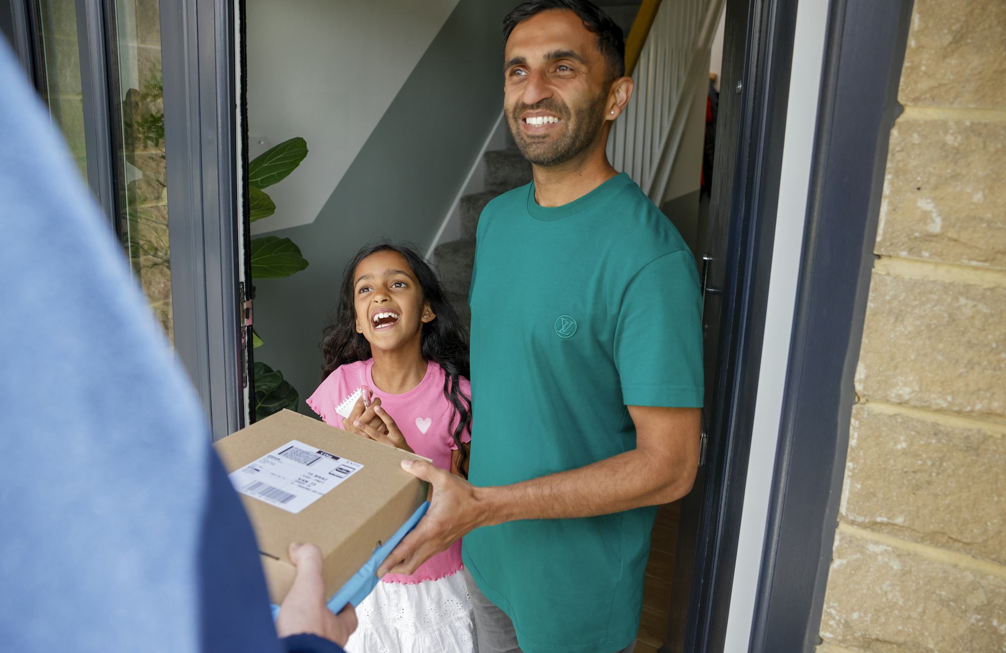 An Evri Courier is handing two parcels to a father and child on their doorstep. They are laughing as if a joke or anecdote was exchanged.