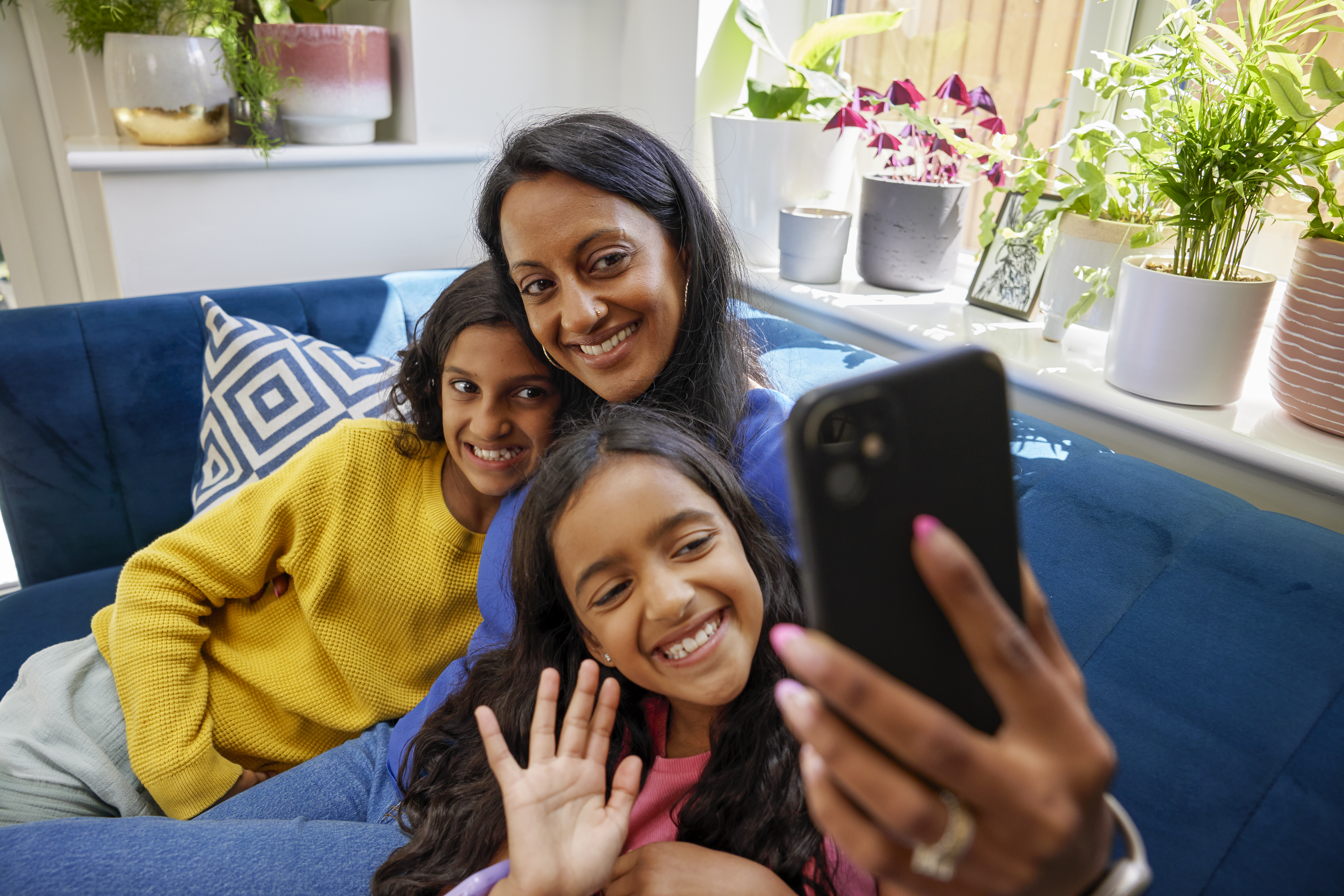 A mother and her two children record an Evri video on their mobile device. They are sat cuddled up on a sofa in their living room.
