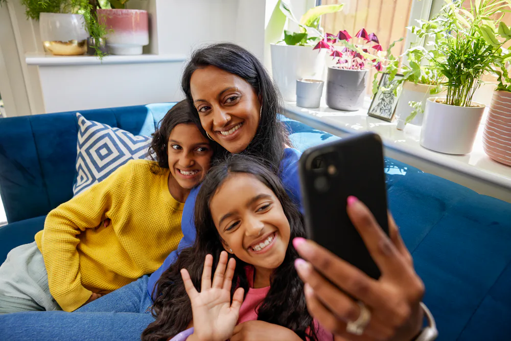 A mother and her two children record an Evri video on their mobile device. They are sat cuddled up on a sofa in their living room.